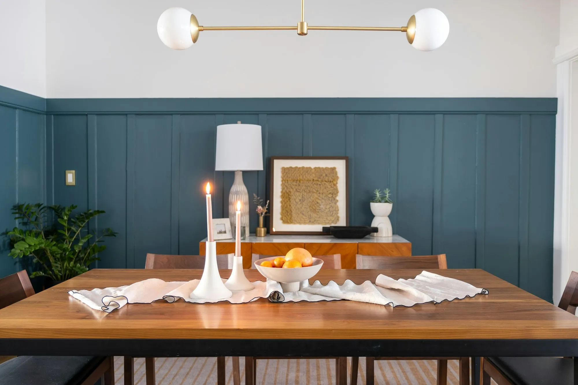 A family dining table set with lit candles and a bowl of oranges