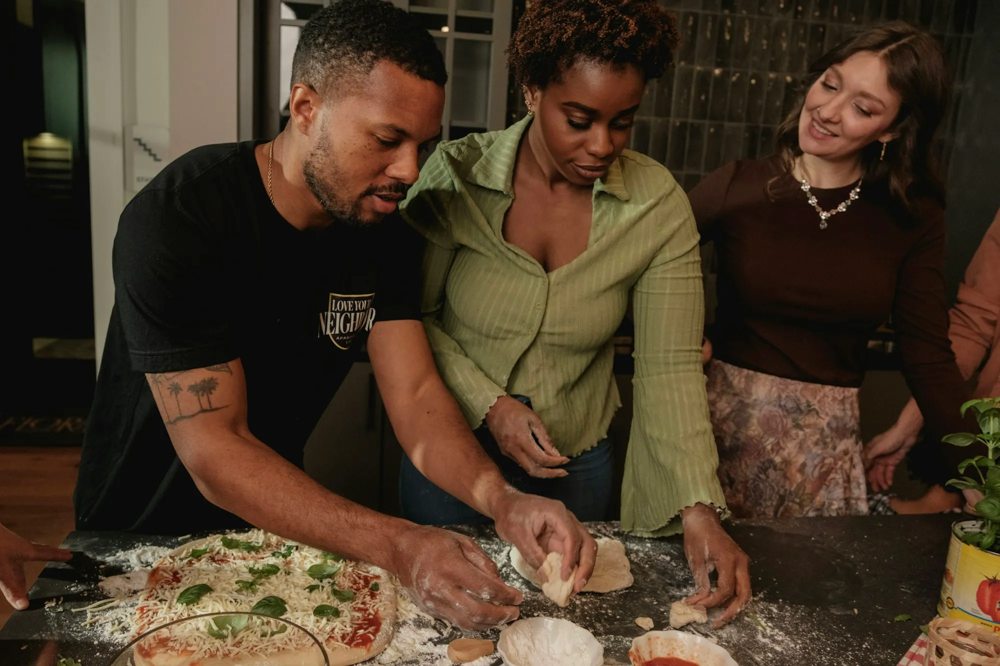 Three young adults making pizza together in a home kitchen